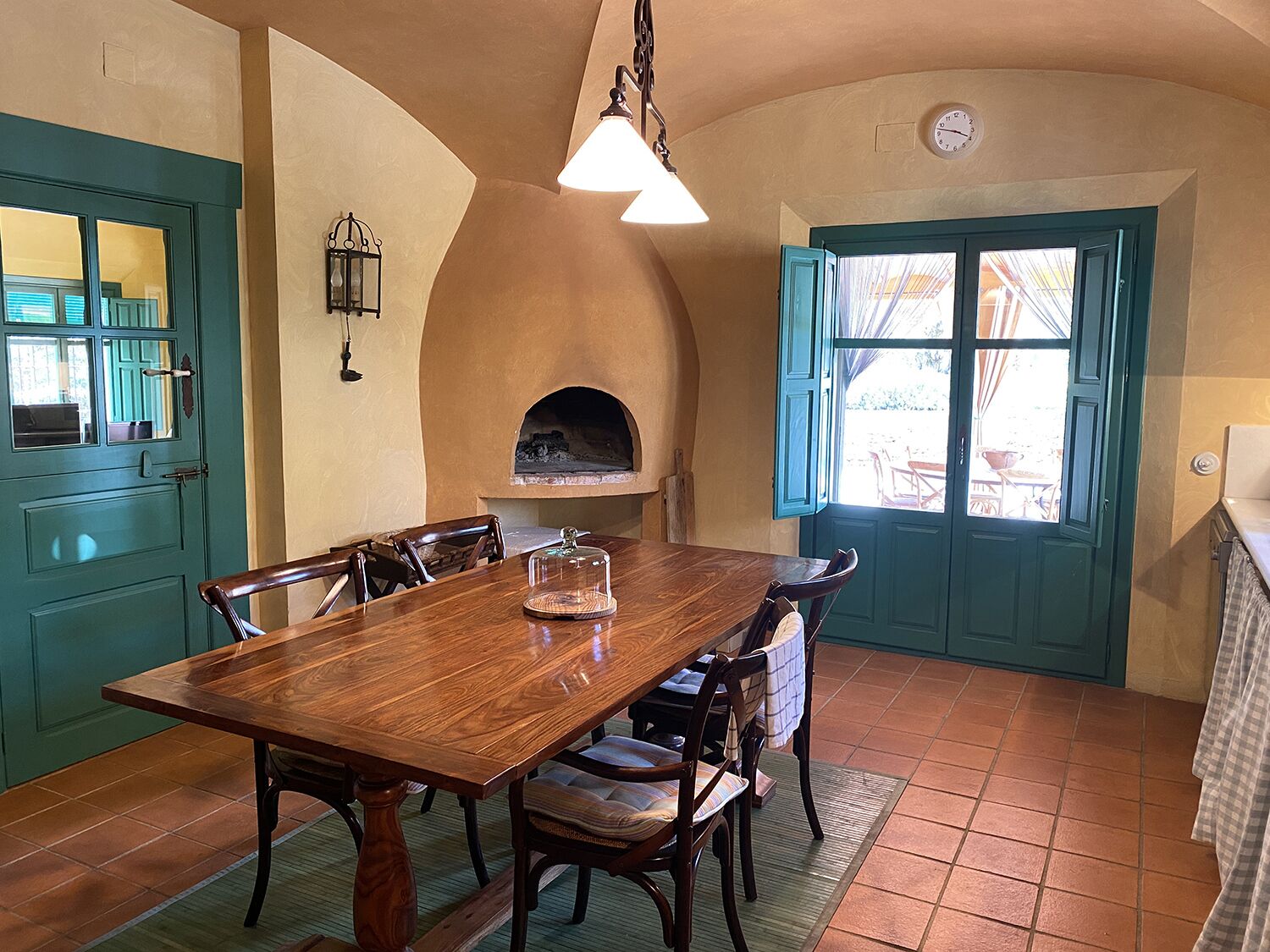 A dining area with a wooden table, chairs, a hanging light fixture, a built-in oven, and a green door with a window.