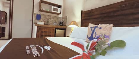 Habitación de hotel con cama, almohada con diseño de ancla, cojín decorativo con estampado de bandera, decoración de mariposa en la pared y una kitchenette.