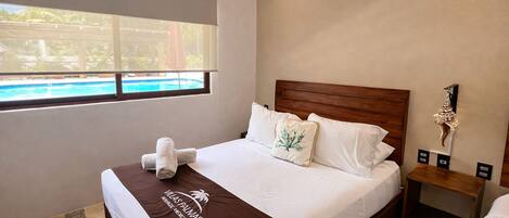 A hotel room with a bed, a nightstand, a window with a view of a pool, and a decorative wall piece.