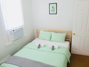 A bedroom with a bed, a window with an air conditioner, a door, and a framed picture on the wall. - BEACH BLOCK - NEW LUXURY CASINO (Atlantic City)