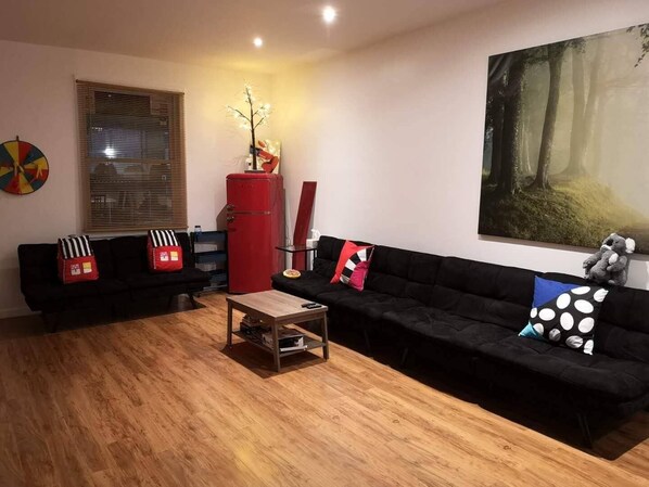 A modern living room with a black sofa, a coffee table, a red cabinet, and a painting of a forest. - BEACH BLOCK - NEW LUXURY CASINO (Atlantic City)