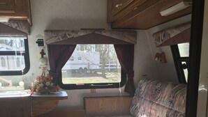 Ein kompaktes Wohnmobil-Interieur mit einer Küchenzeile, einem Bett und einem Fenster mit Blick nach außen.
