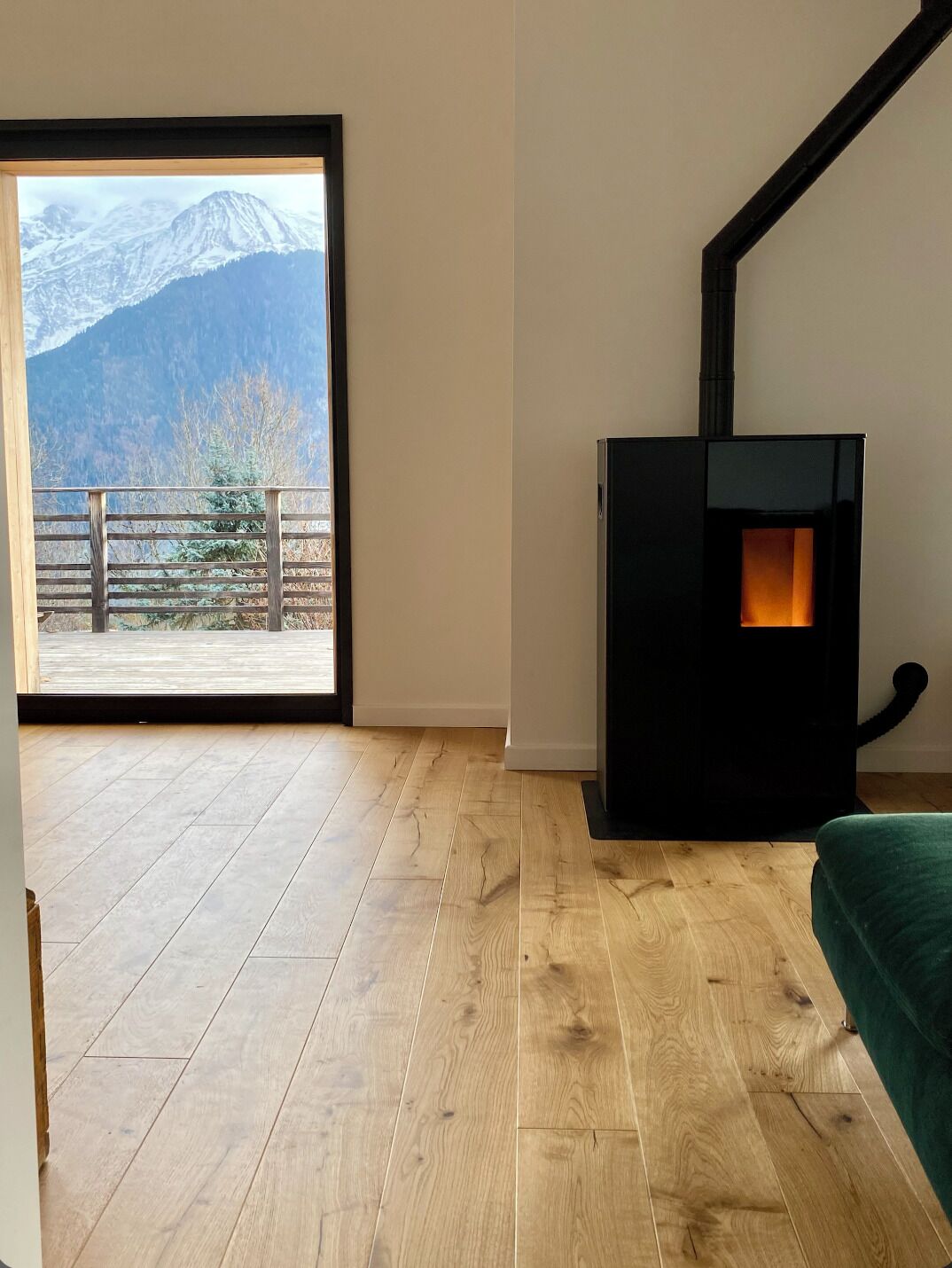 Une pièce dotée d’un plancher en bois, d’une cheminée noire et d’une grande fenêtre donnant sur les montagnes.