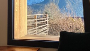 A room with a large window offering a view of snow-capped mountains and a wooden deck outside. - 🏔 Symphonie des Cimes - fully renovated 2024 | Rando & Tennis  (Passy)