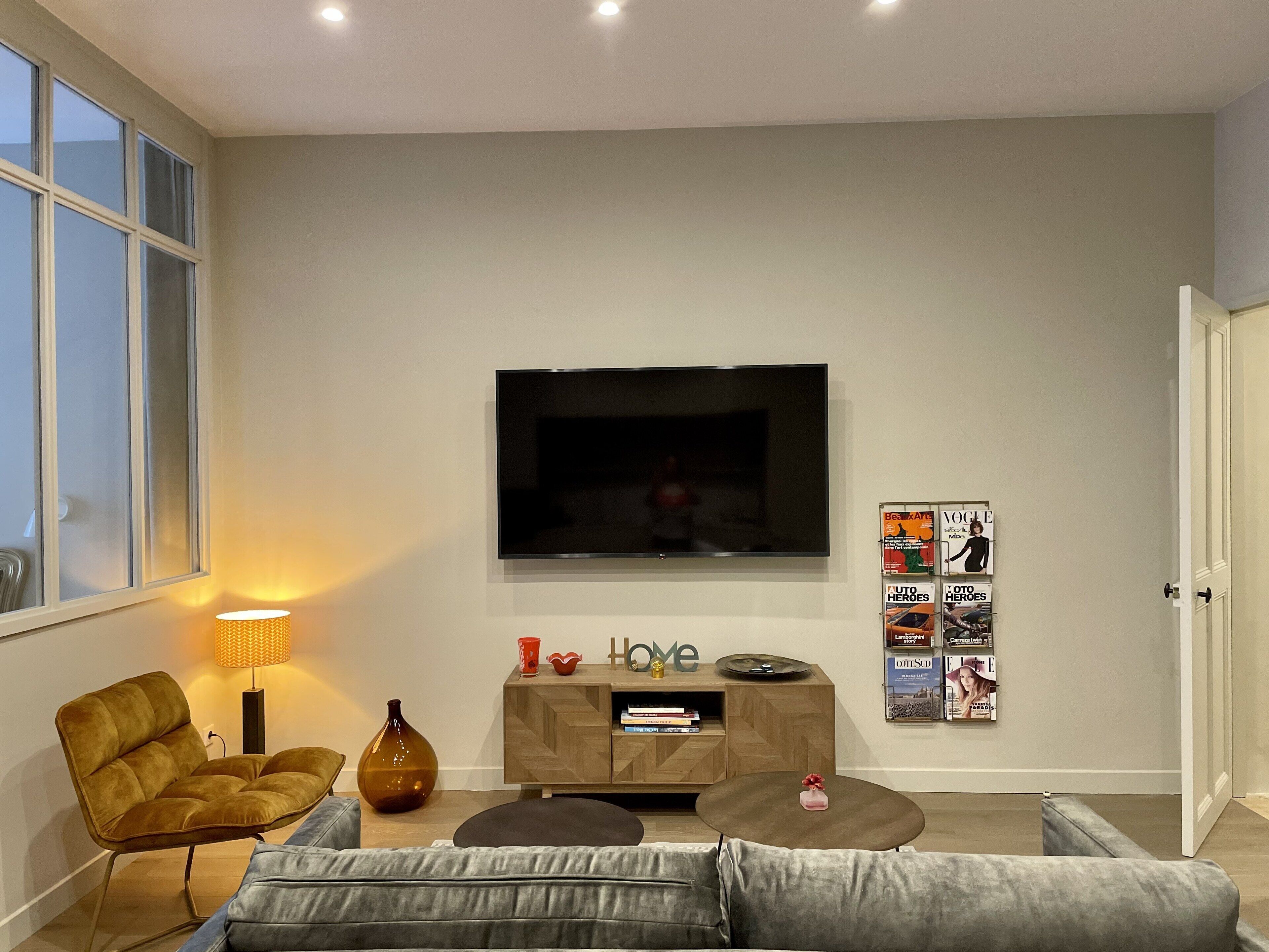 A modern living room with a flat-screen TV, a sofa, a coffee table, a lamp, and a bookshelf.