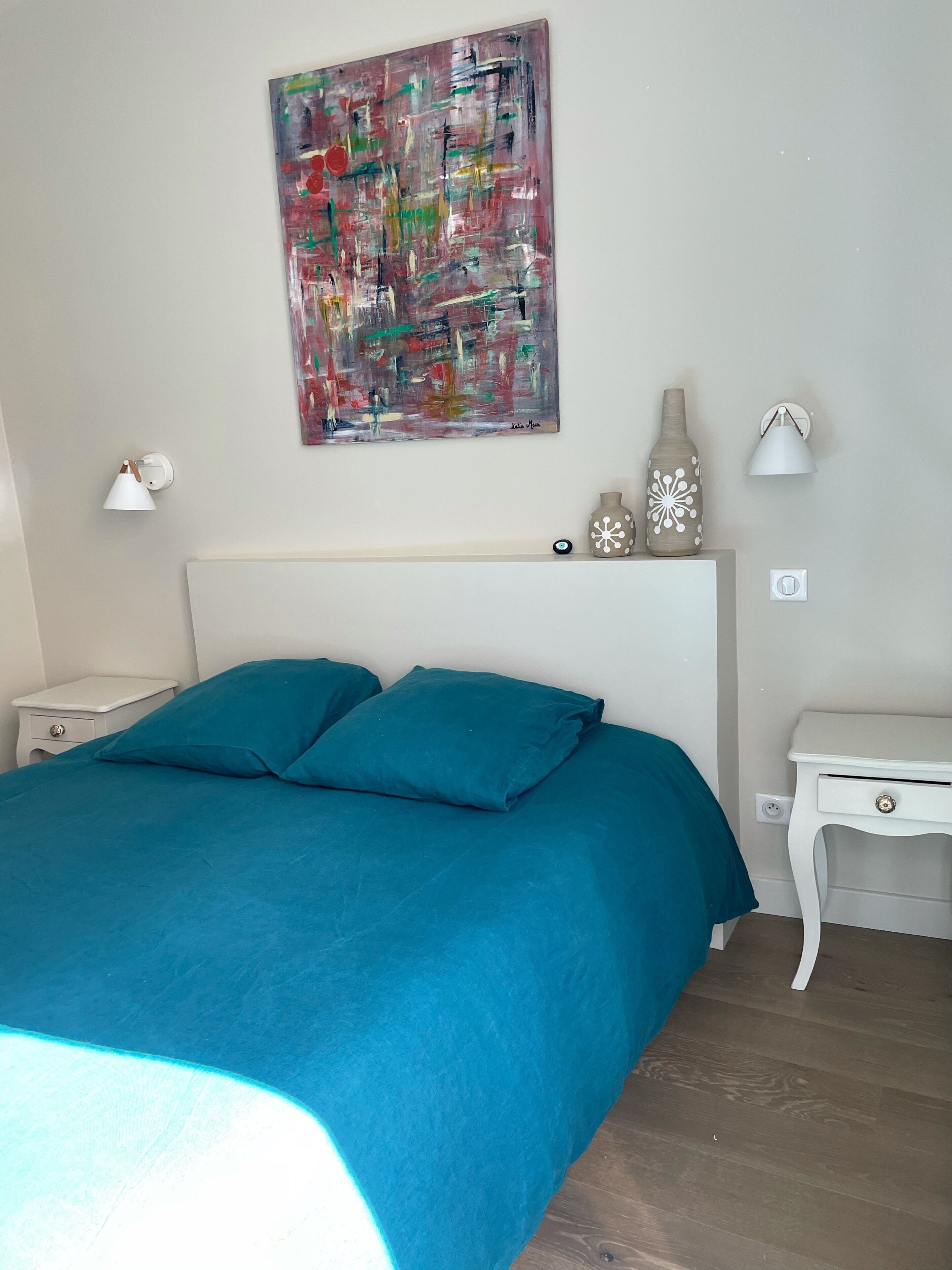 A bedroom with a large bed, a nightstand, a wall-mounted lamp, and a decorative vase.