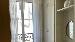 A bedroom with a bed, a chair, a wardrobe, and a window with curtains. - Lappart Hôtel SKA (Saint Rémy de Provence)