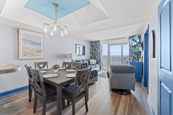 A dining area with a table set for four, a sofa, and a view of the ocean through a large window.