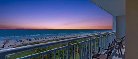 A balcony with a view of a beach and ocean during sunset.