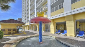 A hotel pool area with a water fountain, lounge chairs, and a building with balconies.