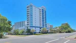 A multi-story hotel with a modern design, featuring balconies, a parking lot, and a clear blue sky. - Horizon Penthouse 18, Lovely Condo in Myrtle Beach (Myrtle Beach)