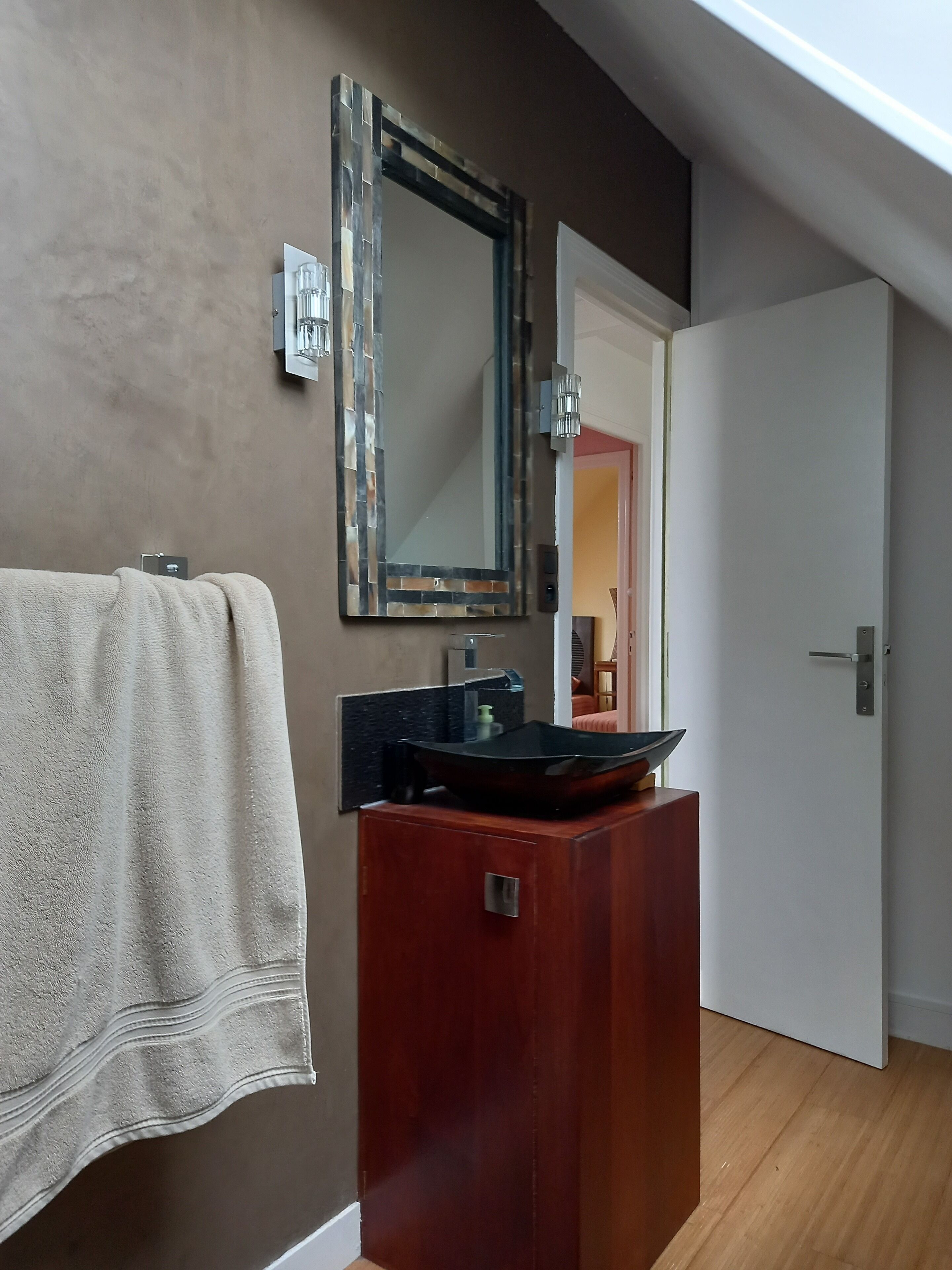 A bathroom with a wooden vanity, a large mirror, and a towel hanging on the wall.