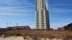 A tall, rectangular hotel with multiple floors and balconies, surrounded by sandy beach and sparse vegetation. - MB Resort Renaissance 514 - OV 2 Bedrooms (Myrtle Beach)
