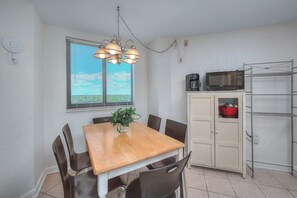 A dining area with a wooden table and chairs, a potted plant, and a kitchen area with a microwave and shelves. - MB Renaissance Tower 904-1BR OF Condo in Myrtle Beach (Myrtle Beach)