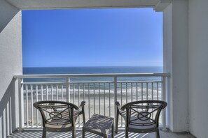 Enjoy the ocean view from this balcony with two chairs and a table.