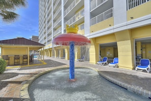 Un espace piscine d’hôtel avec une fontaine, des chaises longues et un bâtiment doté de balcons.