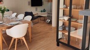 Ein moderner Essbereich mit einem Holztisch, gedeckt für vier Personen, weißen Stühlen, einem an der Wand befestigten Fernseher und einer Vitrine mit Geschirr.