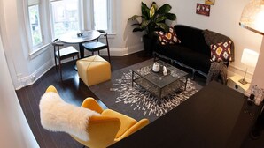 Un salon comprenant un canapé, une table basse, un fauteuil jaune, une table à manger avec des chaises et une grande plante.