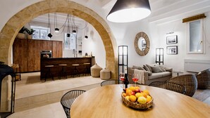 A spacious living area with a wooden dining table, a kitchen in the background, and a large arched doorway. - CharmSuites - charming flat in Ortigia (Siracusa)