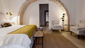 A bedroom with a large arched doorway, a bed with a green throw, a white sofa, a small table, and a floor lamp. - CharmSuites - charming flat in Ortigia (Siracusa)
