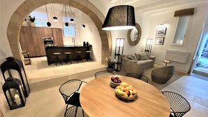 A modern dining area with a round wooden table, black chairs, and a central fruit basket. - CharmSuites - charming flat in Ortigia (Siracusa)
