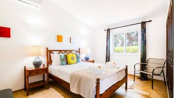 A well-lit bedroom with a wooden bed, two bedside tables, a chair, and a window with curtains.