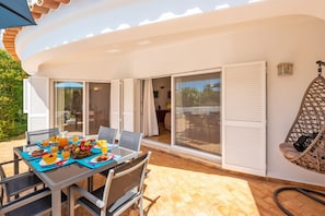 A patio with a table set for breakfast, including fruits and beverages, and a wicker chair.