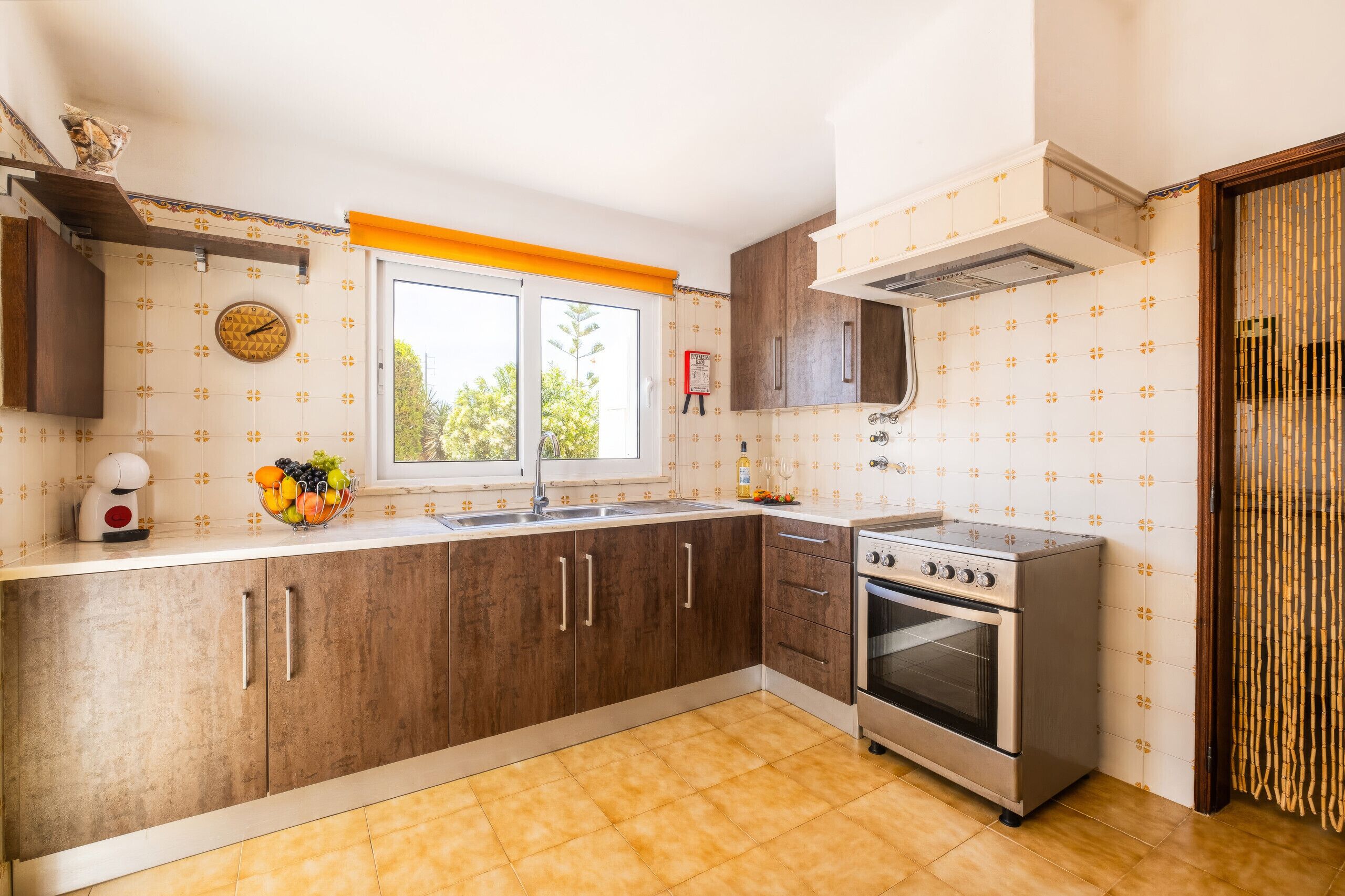 Una cocina con armarios de madera, una estufa de acero inoxidable, una ventana con vistas y un reloj en la pared.