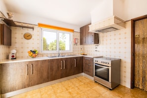 A kitchen with wooden cabinets, a stainless steel stove, a window with a view, and a clock on the wall.