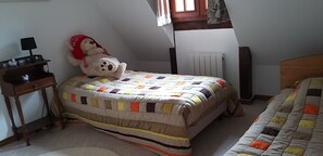 Ein Schlafzimmer mit einem Bett, einem kleinen Schreibtisch mit Lampe, einem Heizkörper und einem Fenster mit Vorhängen.