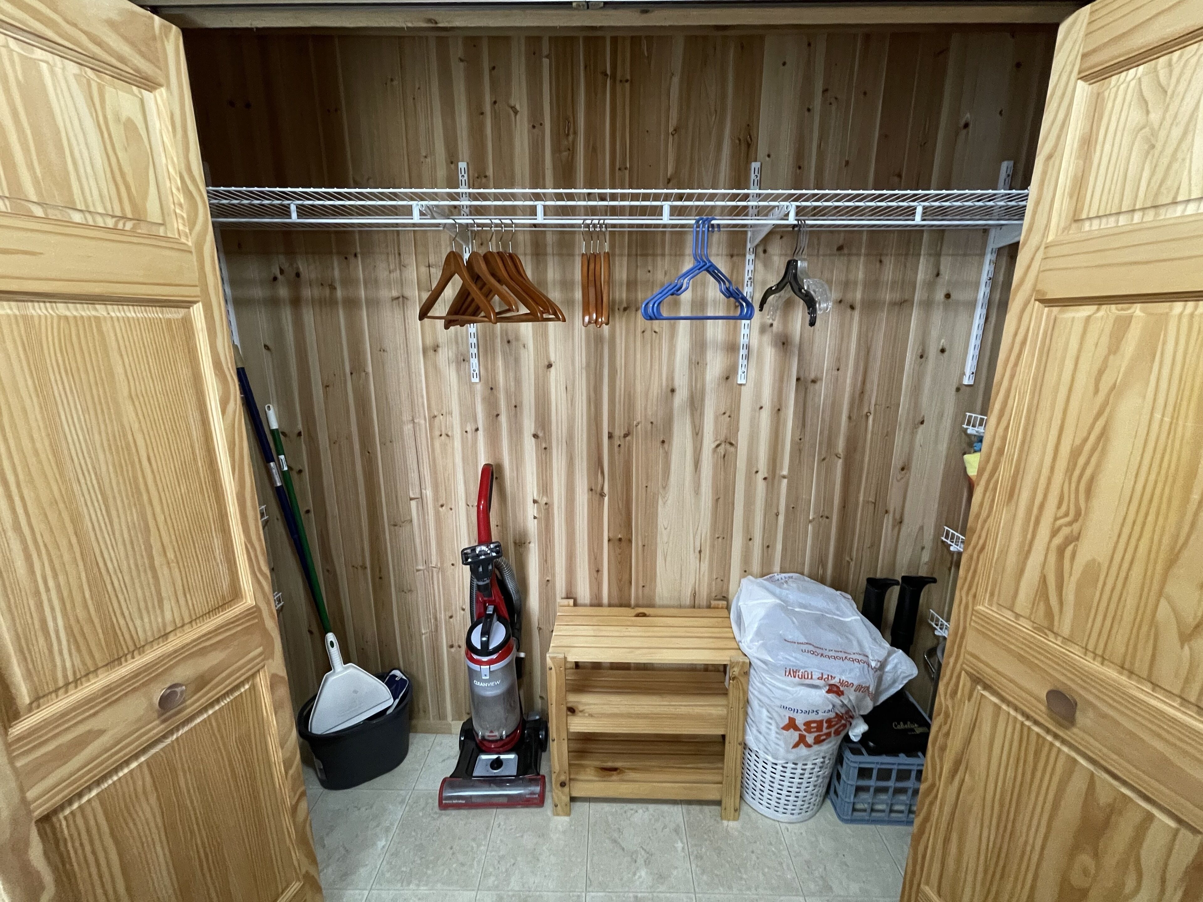 A wooden room with a bench, a vacuum cleaner, a broom, and a trash bin.