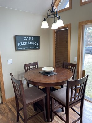 A dining area with a round wooden table, six chairs, a bowl on the table, and a sign on the wall. - Perfect Getaway! Secluded Modern 3 Bedroom, 2 Bath Cabin on 12.5 Private Acres (Baldwin)