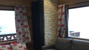 Una habitación acogedora con una pared de acento de piedra, un sofá gris, un banco de madera con cojines estampados con motivos de renos y una pequeña mesa negra.