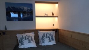 Un dormitorio con cama, dos almohadas decoradas con motivos forestales, una estantería con figuritas de animales y un cuadro de un paisaje nevado.