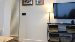 Una sala de estar con televisor, dos cuadros enmarcados, una lámpara y una estantería con cestas.
