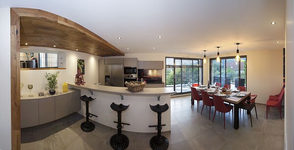 Een moderne keuken met een gebogen kookeiland, barkrukken en een eethoek met rode stoelen.