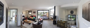Een ruime woonkamer met een grote bank, een salontafel en een open haard. Er is een balkon met uitzicht op de omgeving.