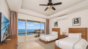 Ein Hotelzimmer mit zwei Betten, einem Deckenventilator, einem Fernseher und Meerblick.