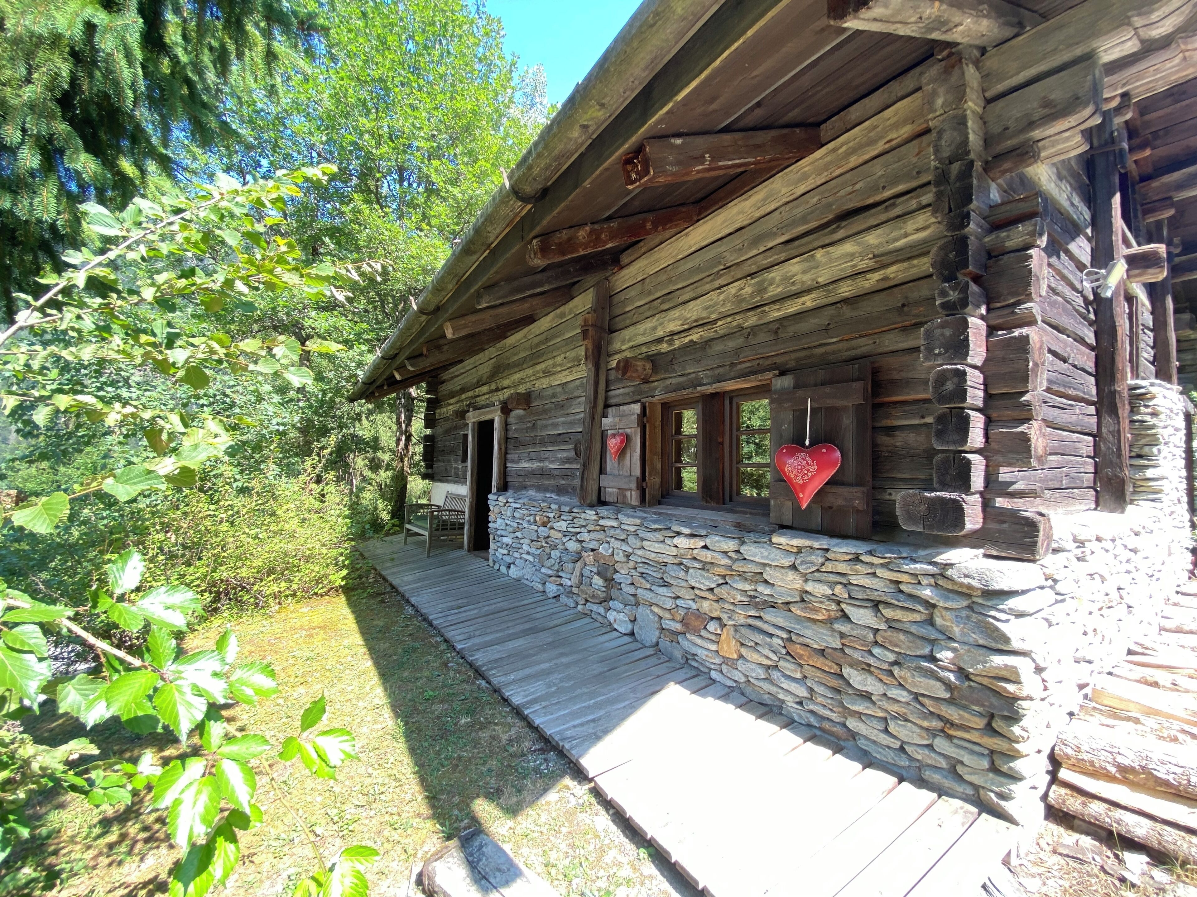 Une cabane rustique en rondins de bois, avec des fondations en pierre, une véranda en bois et des décorations en forme de cœur.