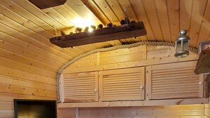 A cozy cabin interior with a wooden interior, a sofa with cushions, a small table with a reindeer design, and a hanging lantern. - Gemütlicher Schäferwagen in der Eifel (Nettersheim)