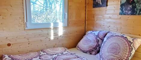 A wooden cabin room with a bed, a window, and a wall-mounted light fixture.