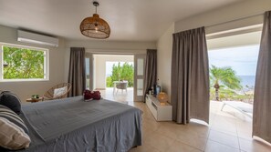 A bedroom with a bed, a chair, a small table, and a view of the outdoors. - Villa Summertime - Coral Estate Resort (Coral Estate)
