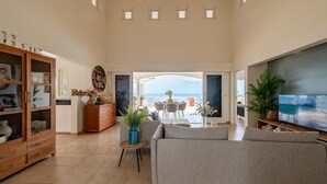 Een ruime woonkamer met uitzicht op zee, een houten kast, een bank en een televisie.