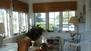 Ein gemütliches Zimmer mit Korbmöbeln, einem Bücherregal und Blick ins Freie.