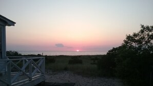Blick auf einen Strand mit einer Holzkonstruktion, einem Sandweg und einem Sonnenuntergang über dem Meer.