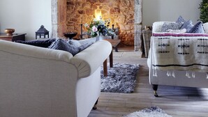 Ein gemütliches Wohnzimmer mit Kamin aus Stein, einer Kristallleuchter und einer bequemen Couch.