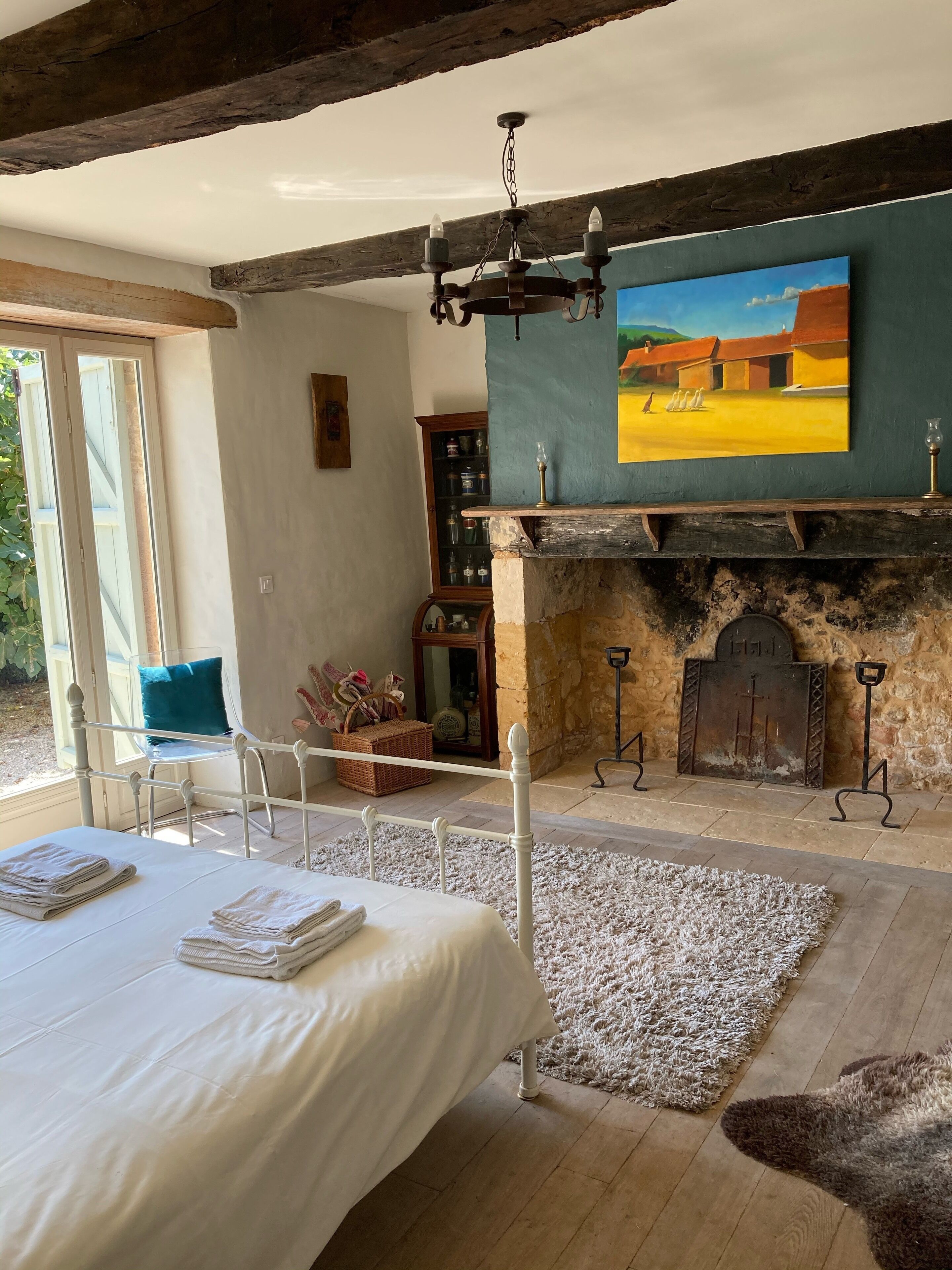 Um quarto com cama, lareira, pintura e vista para o exterior.