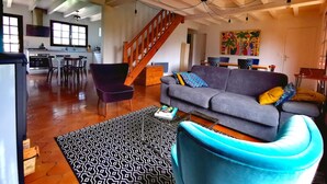 Un amplio salón con un sofá, un tapete estampado y un sillón azul. Una escalera conduce a un nivel superior.