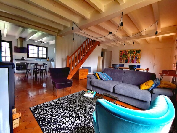 A spacious living area with a sofa, a patterned rug, and a blue chair. A staircase leads to an upper level.