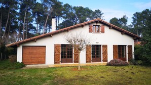 Una casa de dos pisos con fachada blanca, contraventanas de madera y techo inclinado.